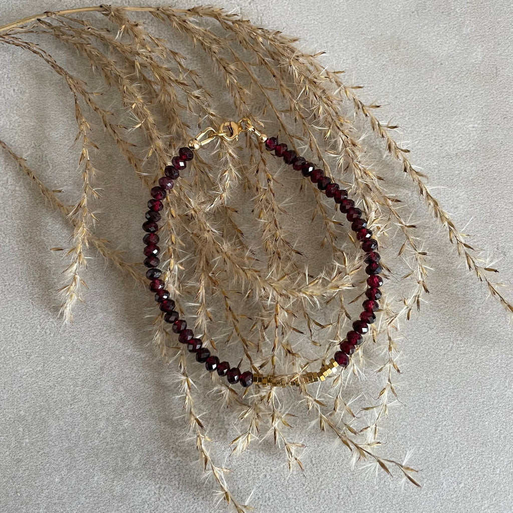 garnet and gold hematite bracelet with 14k rolled gold fittings,  on a beige surface with dried plants