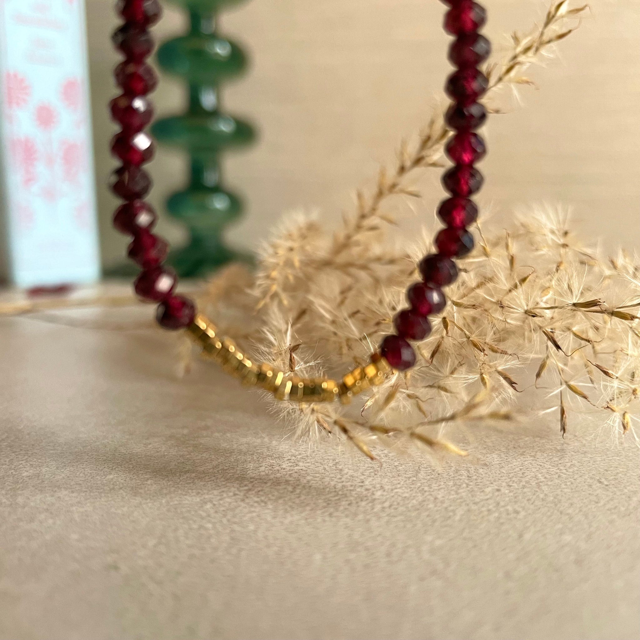 garnet and gold hematite bracelet with 14k rolled gold fittings,  on a beige surface with dried plants