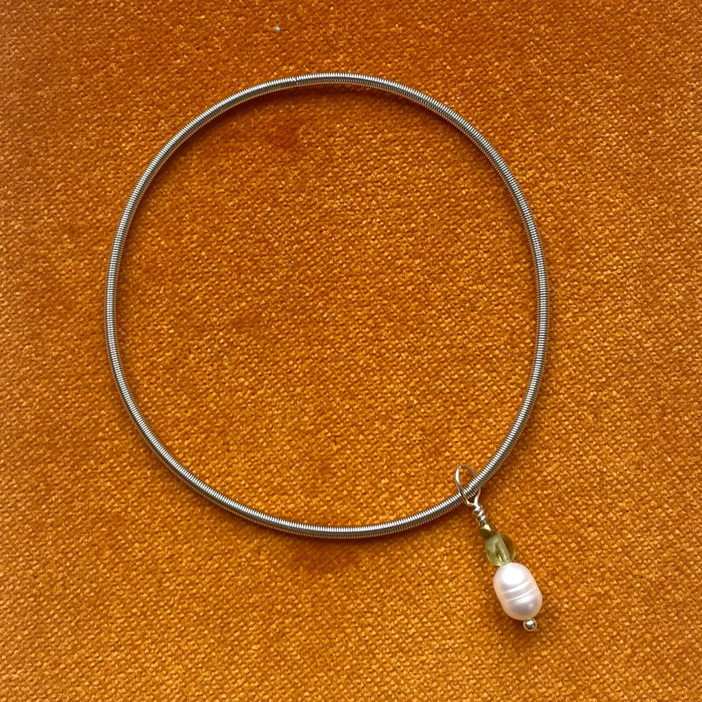 silver wire elasticated bracelet with pearl and peridot charm in orangebackground