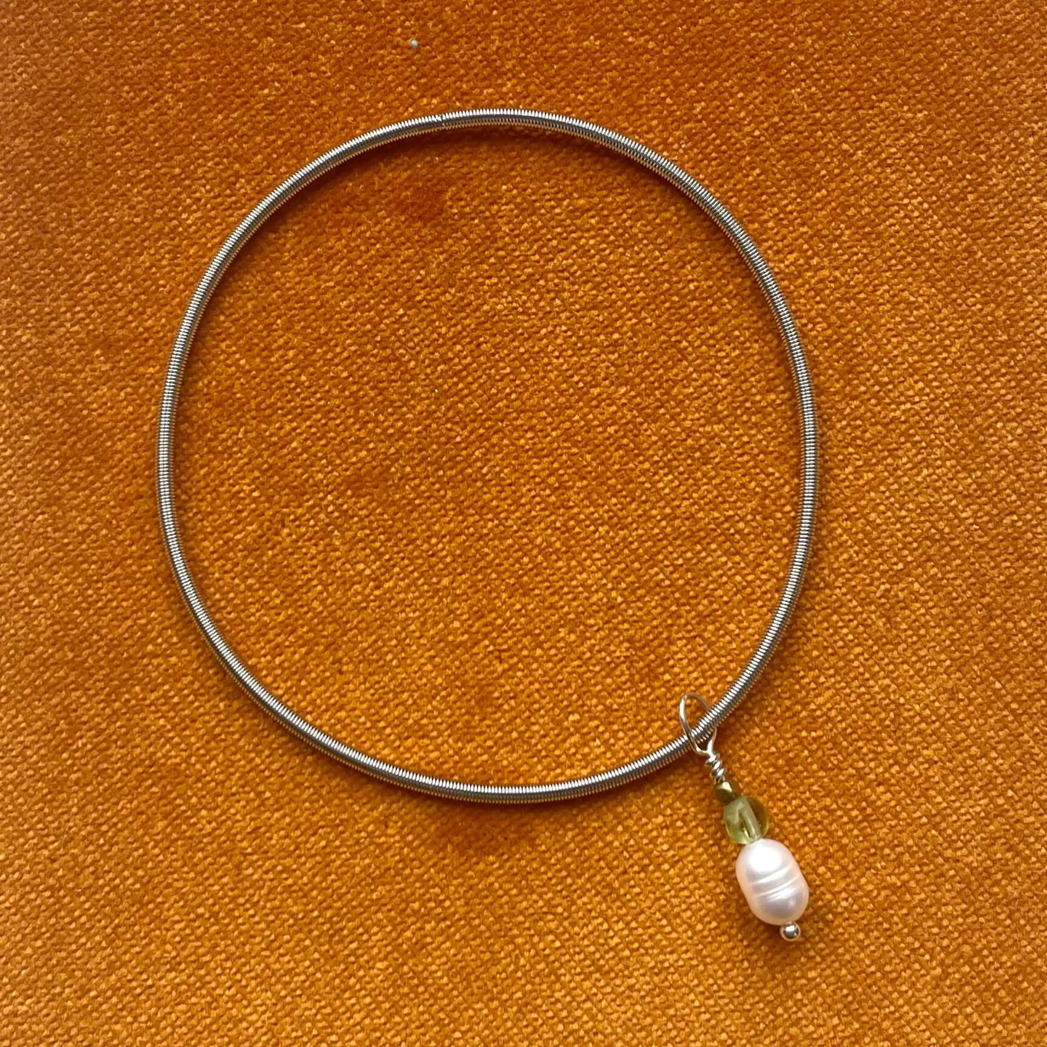 silver wire elasticated bracelet with pearl and peridot charm in orangebackground