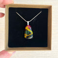 hand-crafted fused glass pendant. colourful fused glass, rich cherry red, yellow, mustard, green. on sterling silver snake chain, complete one-off, only one available, hand holing a jewellery box with pendant inside.