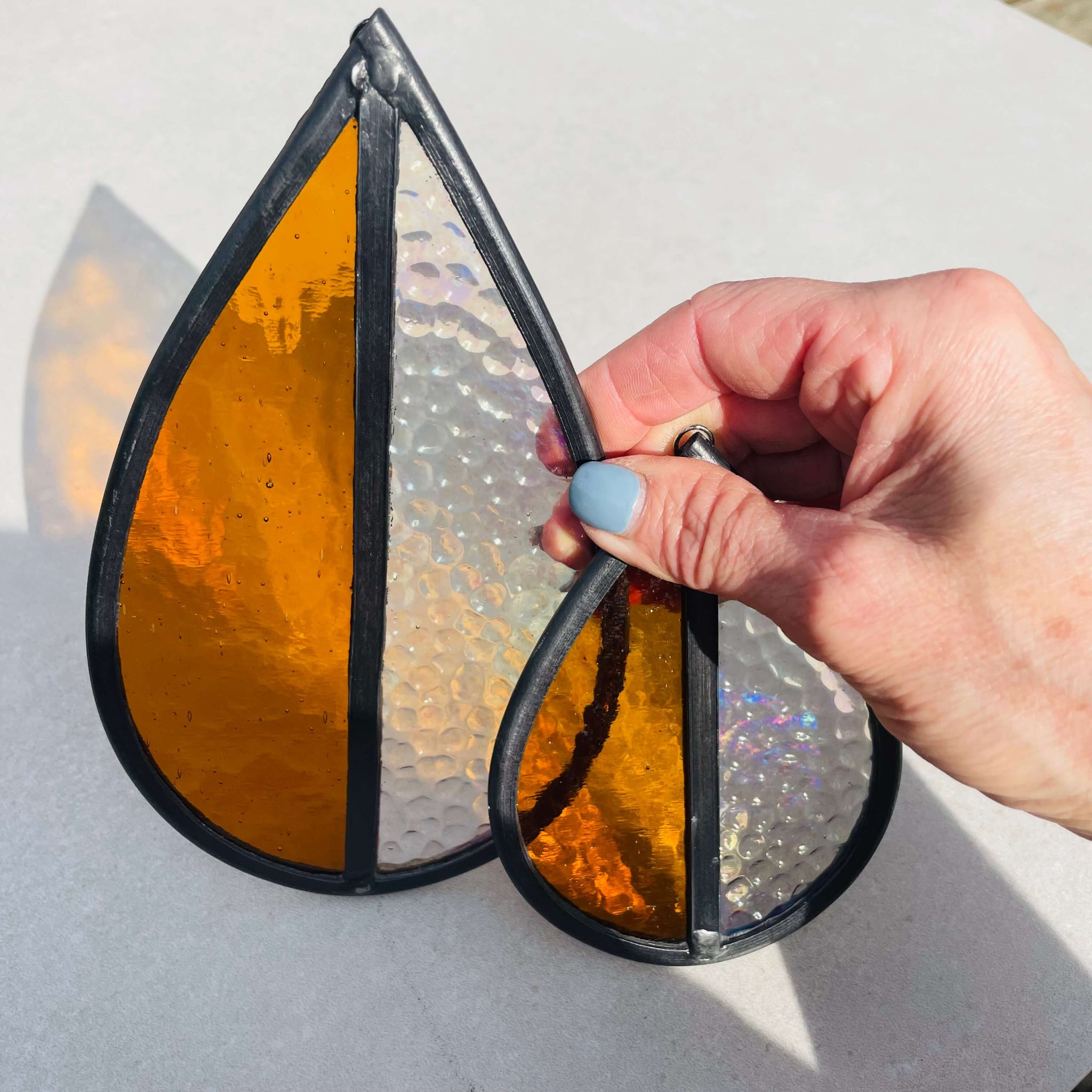 Hand holding a Stained glass medium and small, orange and clear glass sun catcher on a light gray background