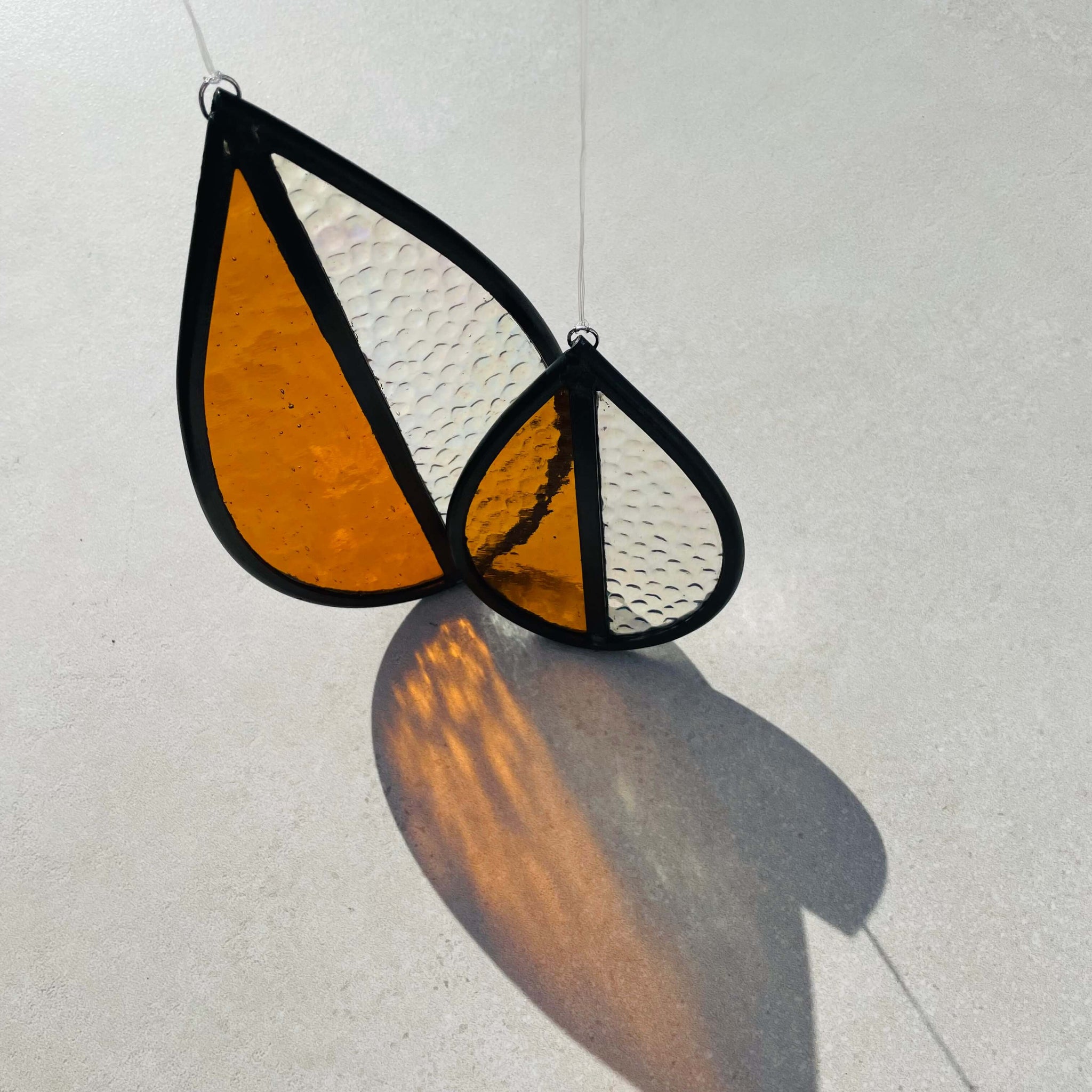 Stained glass medium and small, orange and clear glass sun catcher on a light gray background