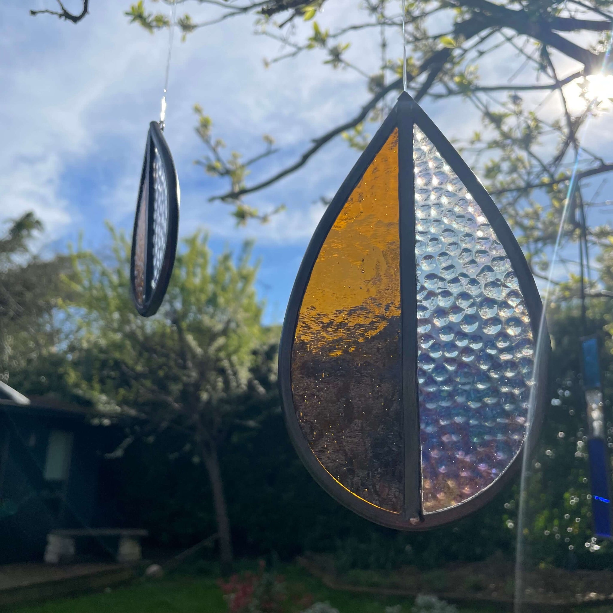 Decorative  Stained glass medium and small, orange and clear glass sun catcher 
glass hanging with a textured surface in a garden setting