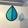 Teardrop-shaped stained glass garden tree spinner / in house sun catcher, with aqua and blue stained glass sections hanging against a white background