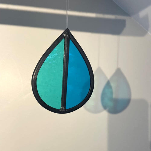 Teardrop-shaped stained glass garden tree spinner / in house sun catcher, with aqua and blue stained glass sections hanging against a white background