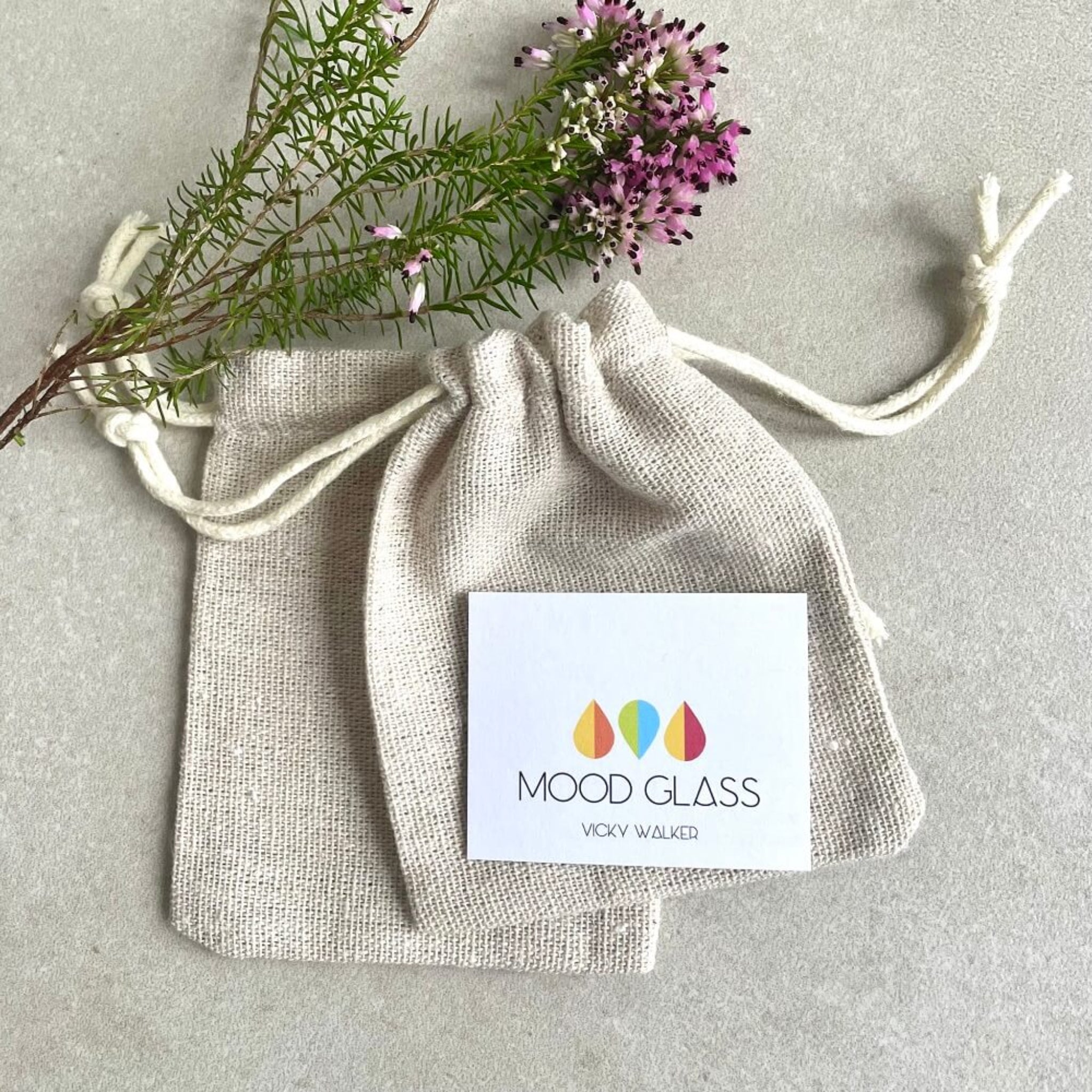 Mood Glass branded linen pouch with heather, purple flowers on a light cream background