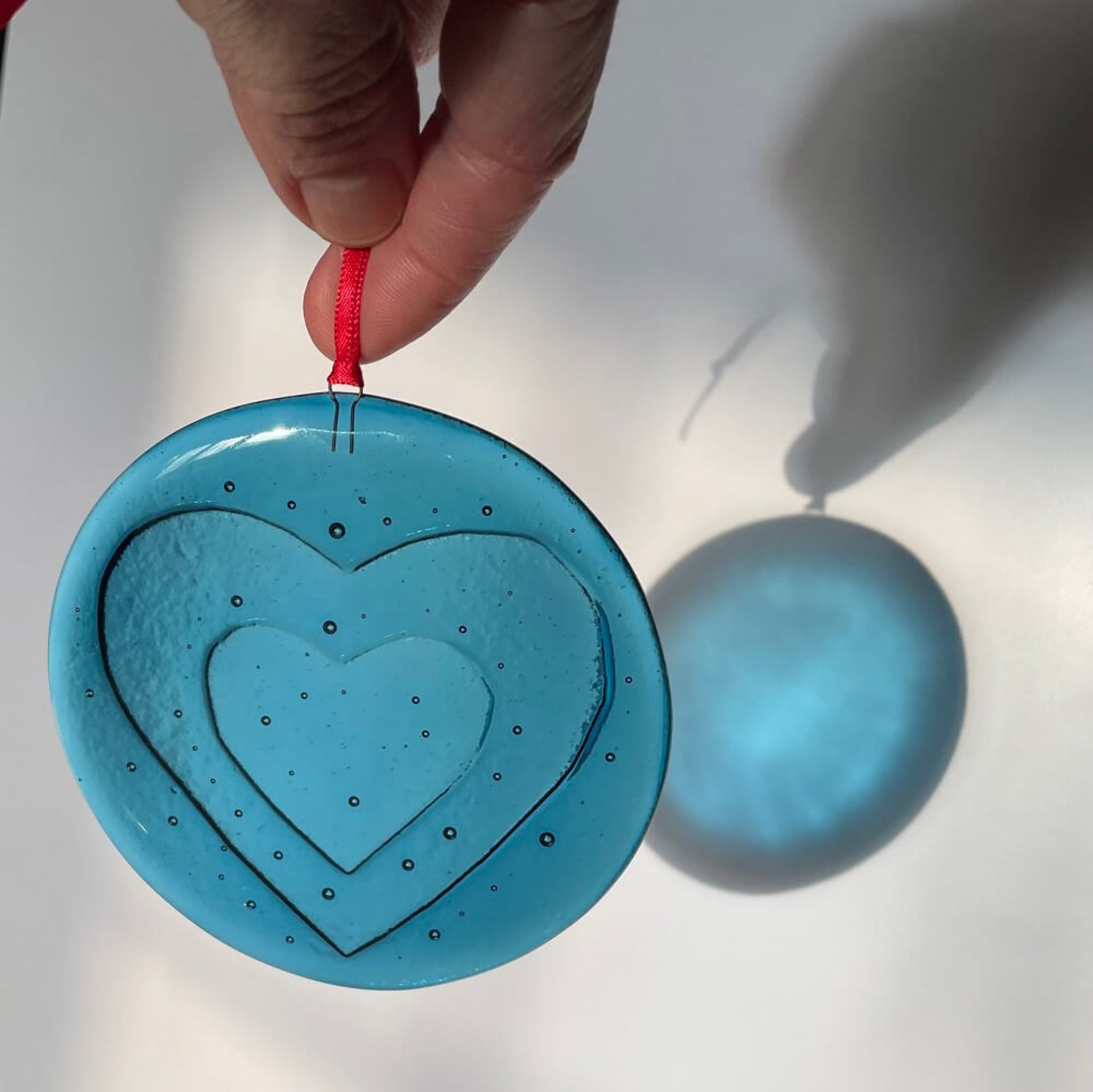 fused glass 'love bomb' Blue heart-shaped hanging decoration, ornament with a red string on a white background