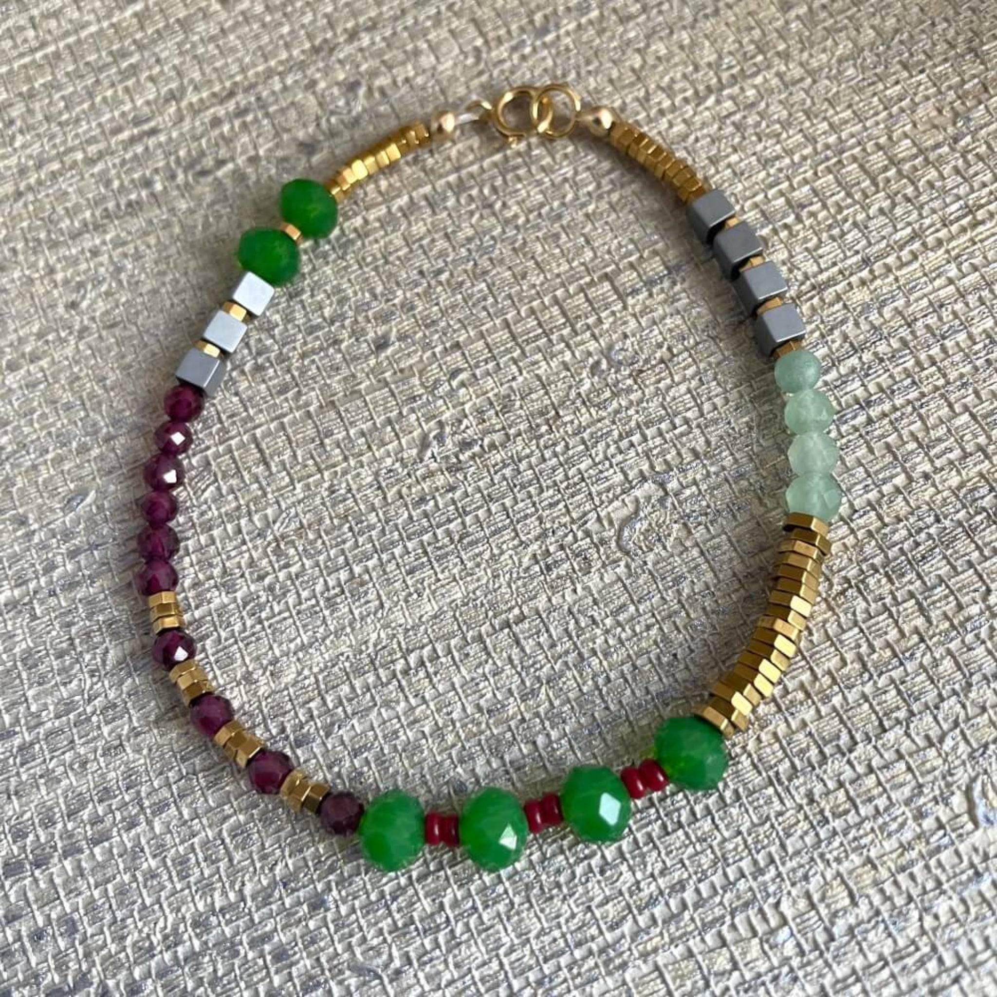 Beaded bracelet with green, red, and gold beads on a textured surface, green, pink, glass beads,  red garnet, golden hematite beads on 14k rolled gold  findings, 