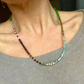 woman wearing fawn coloured jumper, wearing a necklace with multi-coloured beads, red garnet gold and silver hematite, green and aqua faceted glass beads, with 14k rolled gold findings