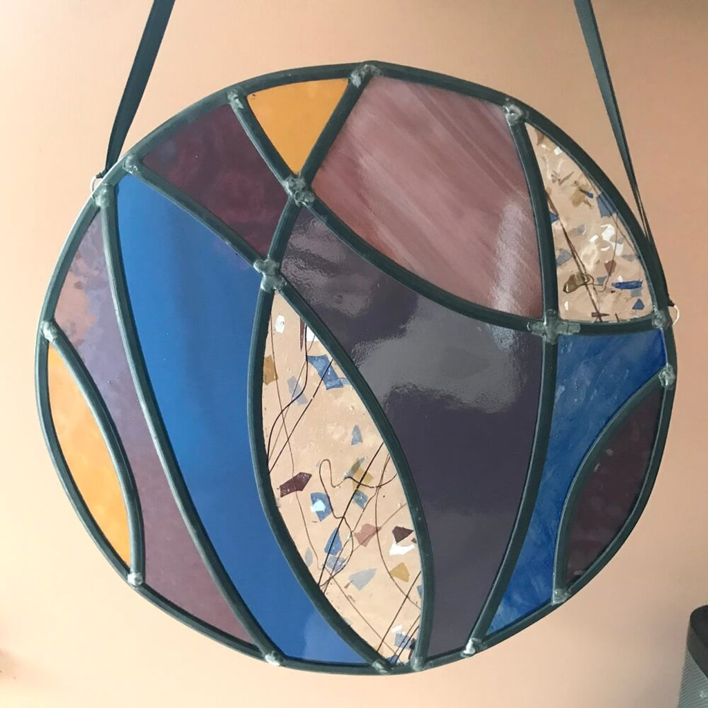 Large stained glass art panel, hanging panel, colourful curved shapes of stained glass, purple, violet, blue, yellow glass,  hanging against a terracotta colour background