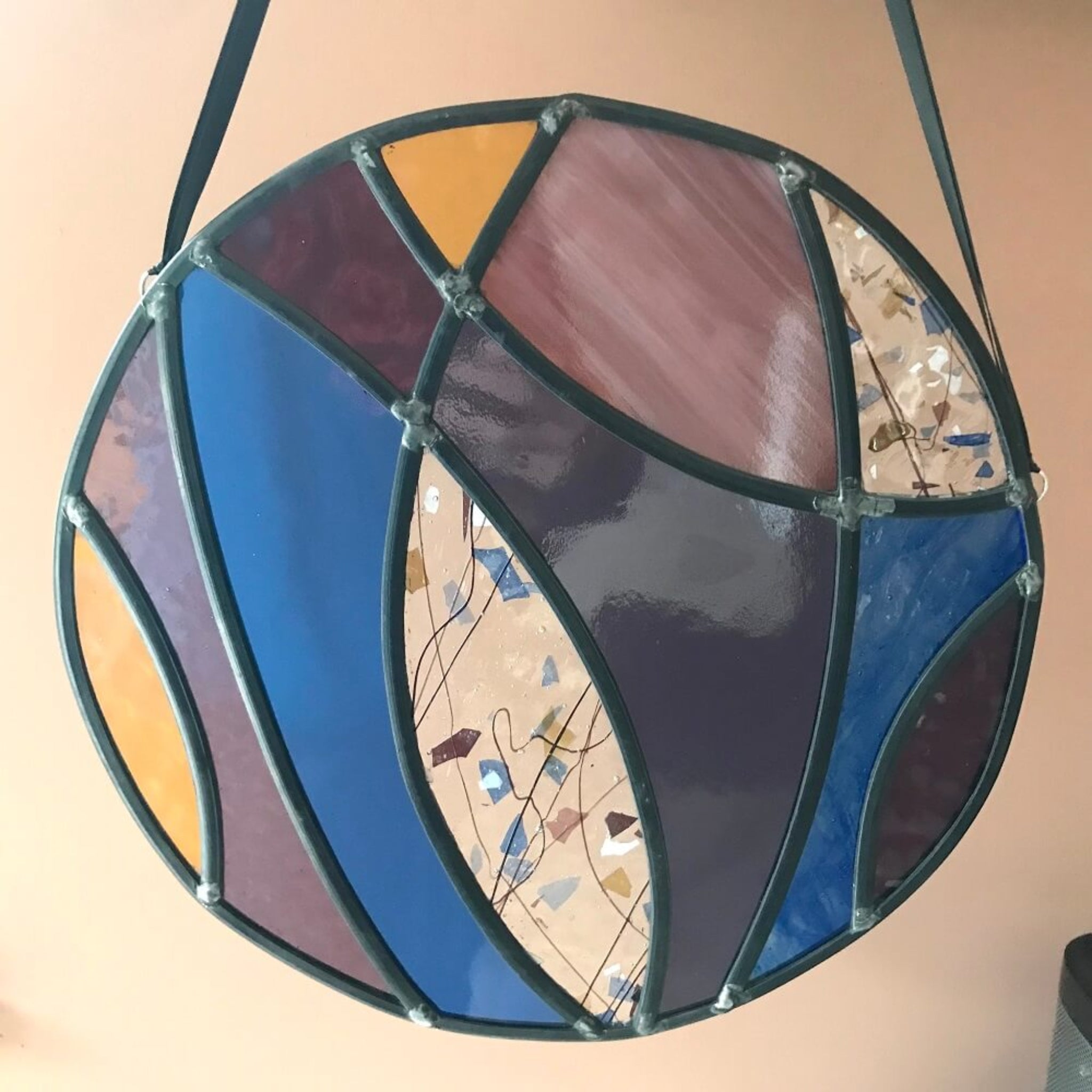 Large stained glass art panel, hanging panel, colourful curved shapes of stained glass, purple, violet, blue, yellow glass,  hanging against a terracotta colour background