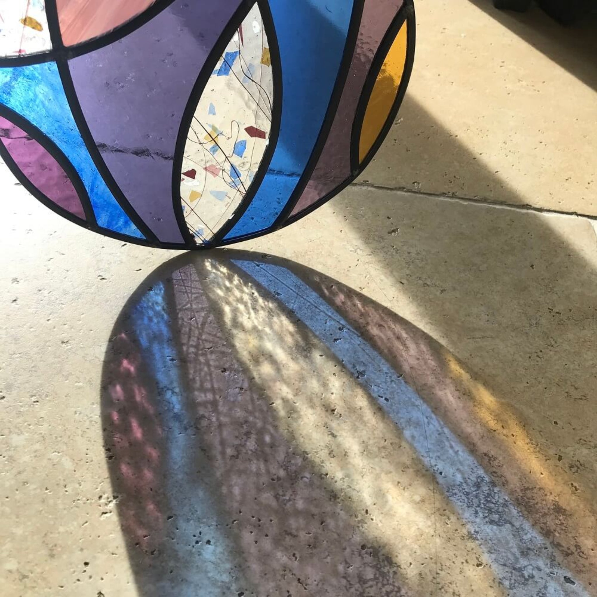 Large stained glass art panel, hanging panel, colourful curved shapes of stained glass, purple, violet, blue, yellow glass,  sunlight refracting through the glass onto a stone floor
