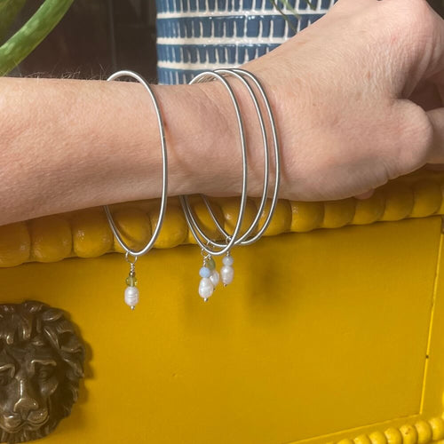 arm wearing 4 Silver elasticated wire charm bracelets with pearls peridot on a bright yellow background