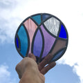 stained glass disk panel artwork, curved shapes of glass, blue and purples, hand holding up to sky.