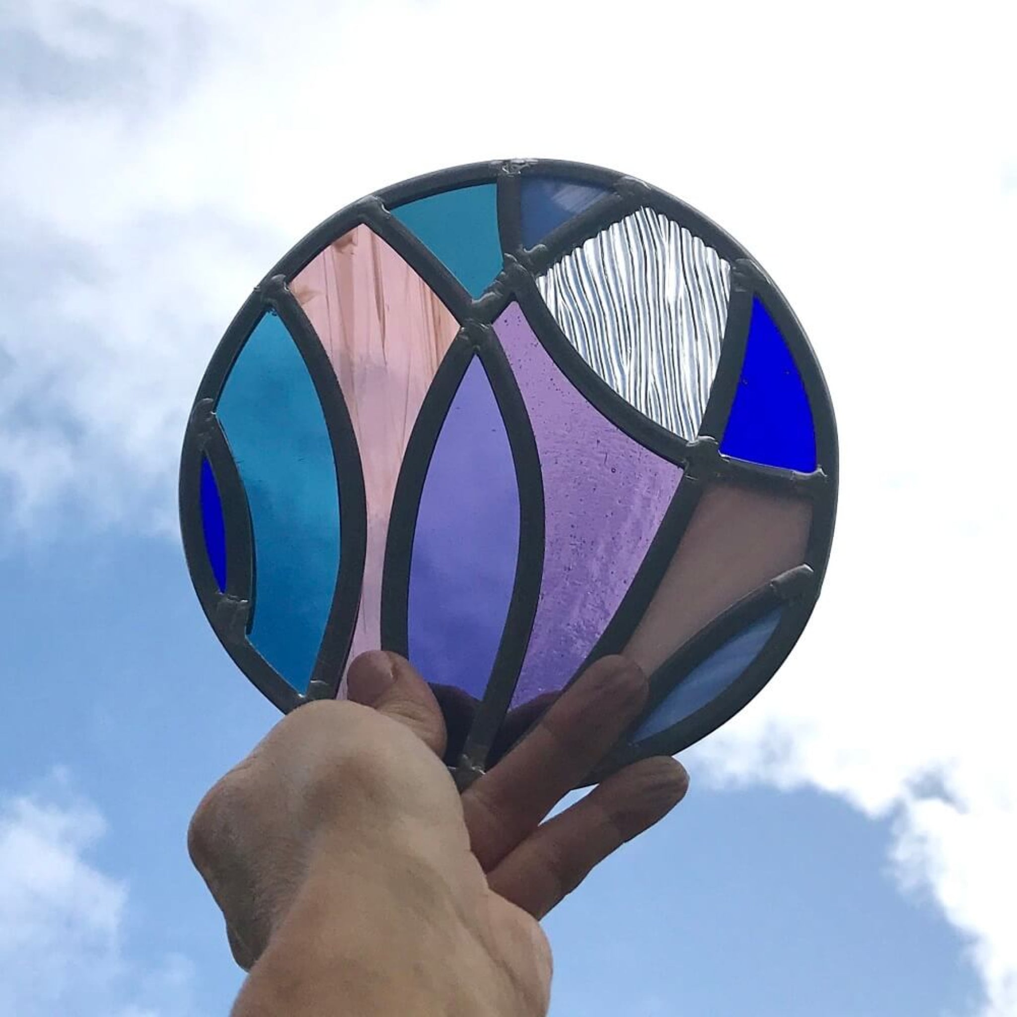 stained glass disk panel artwork, curved shapes of glass, blue and purples, hand holding up to sky.