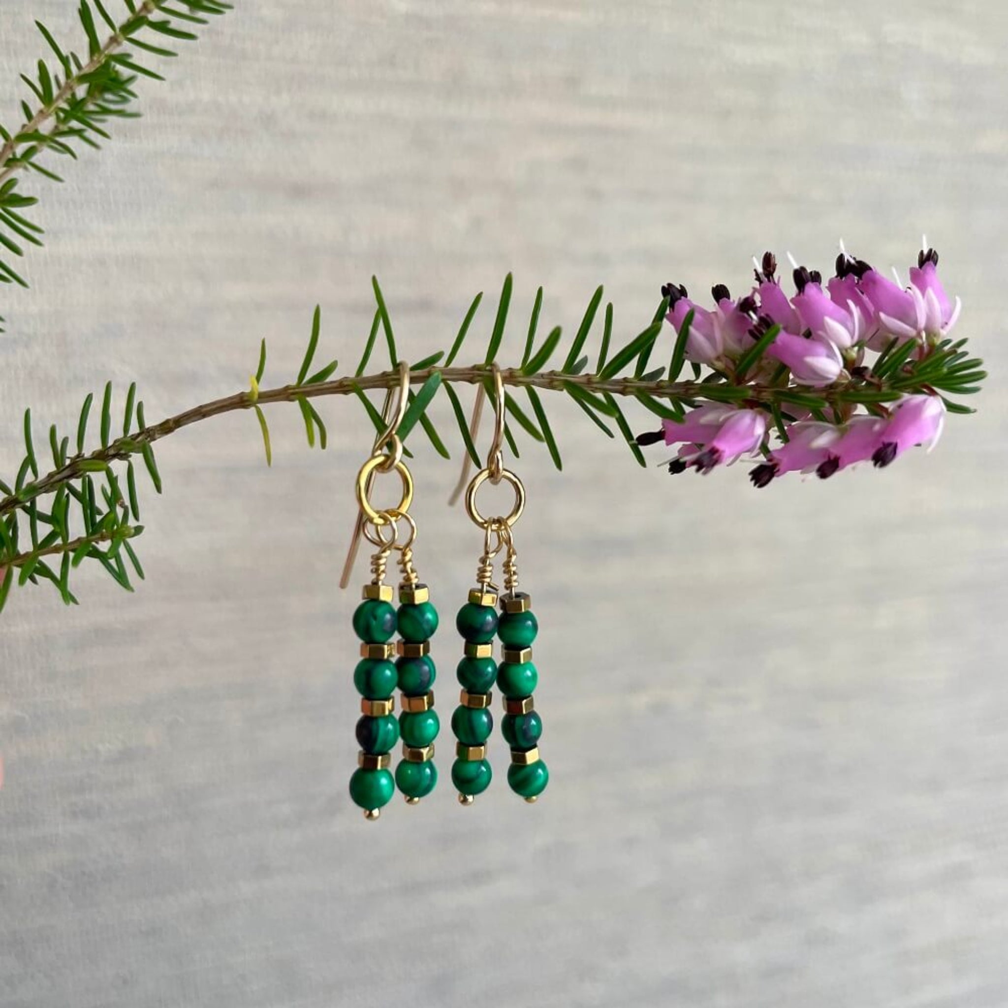 Green beaded malachite and gold hematite earrings on a branch with pink flowers