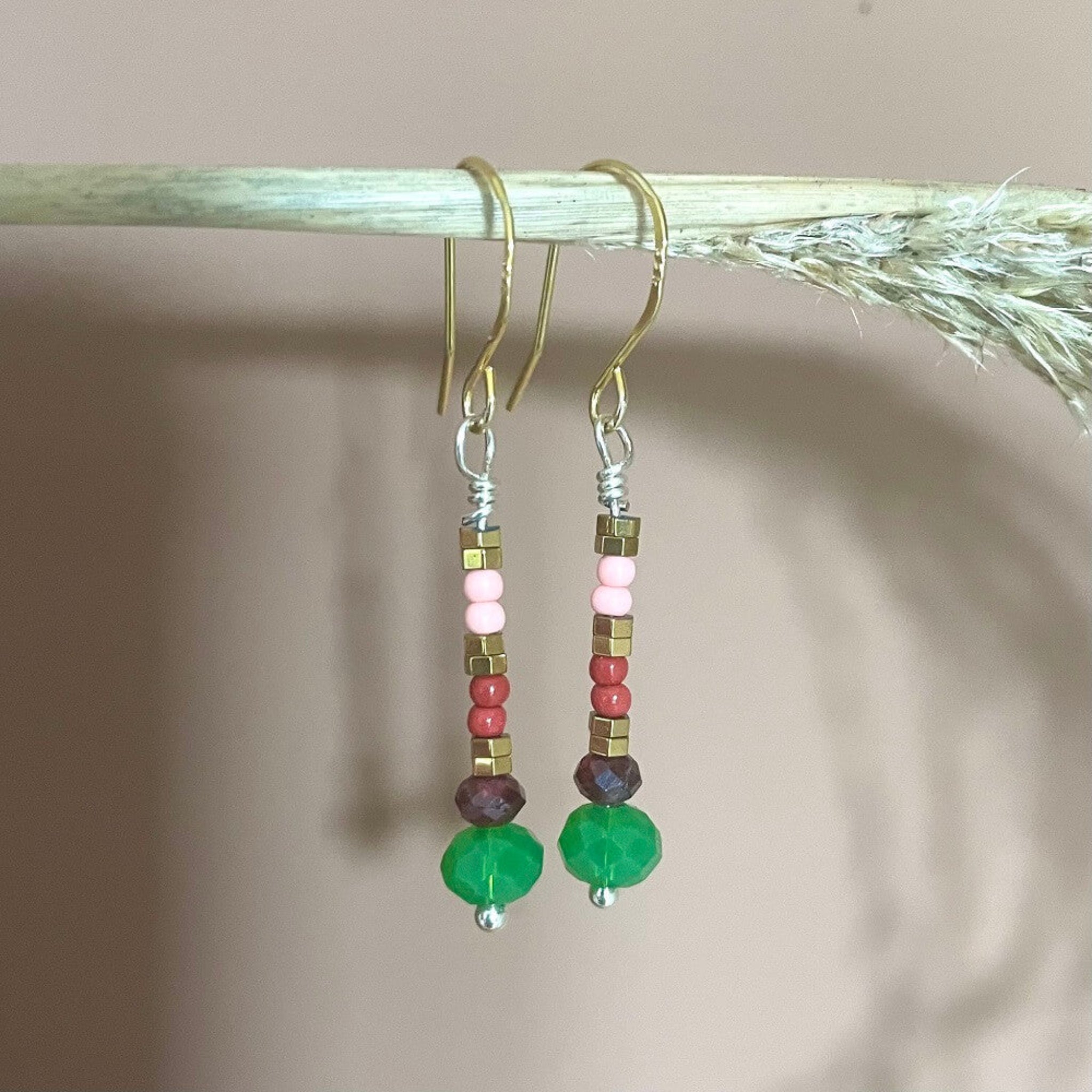 Beaded earrings, green, pink, glass beads,  red garnet, golden hamatite beads on gold vermeil earring hooks, hanging on a twig, pink background
