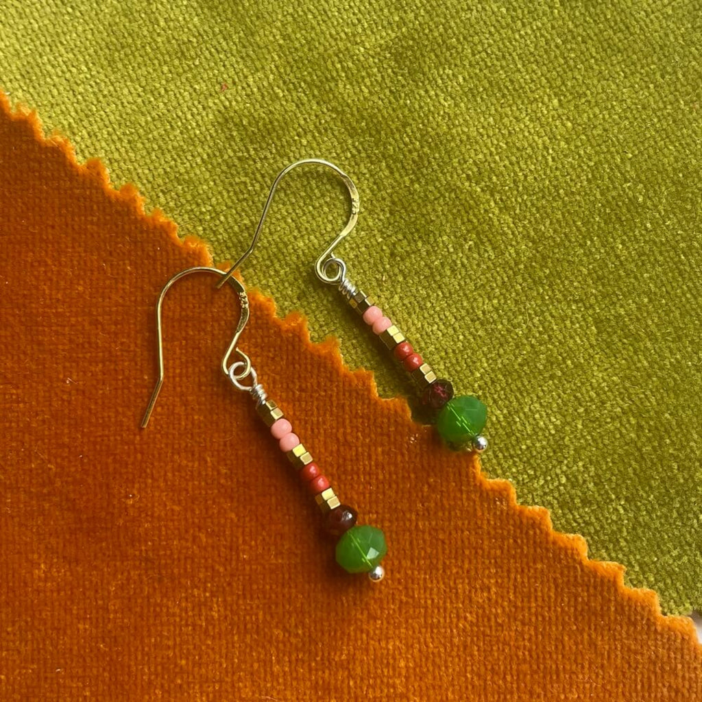 Beaded earrings, green, pink, glass beads,  red garnet, golden hamatite beads on gold vermeil earring hooks, pink background on a textured orange and green fabric background