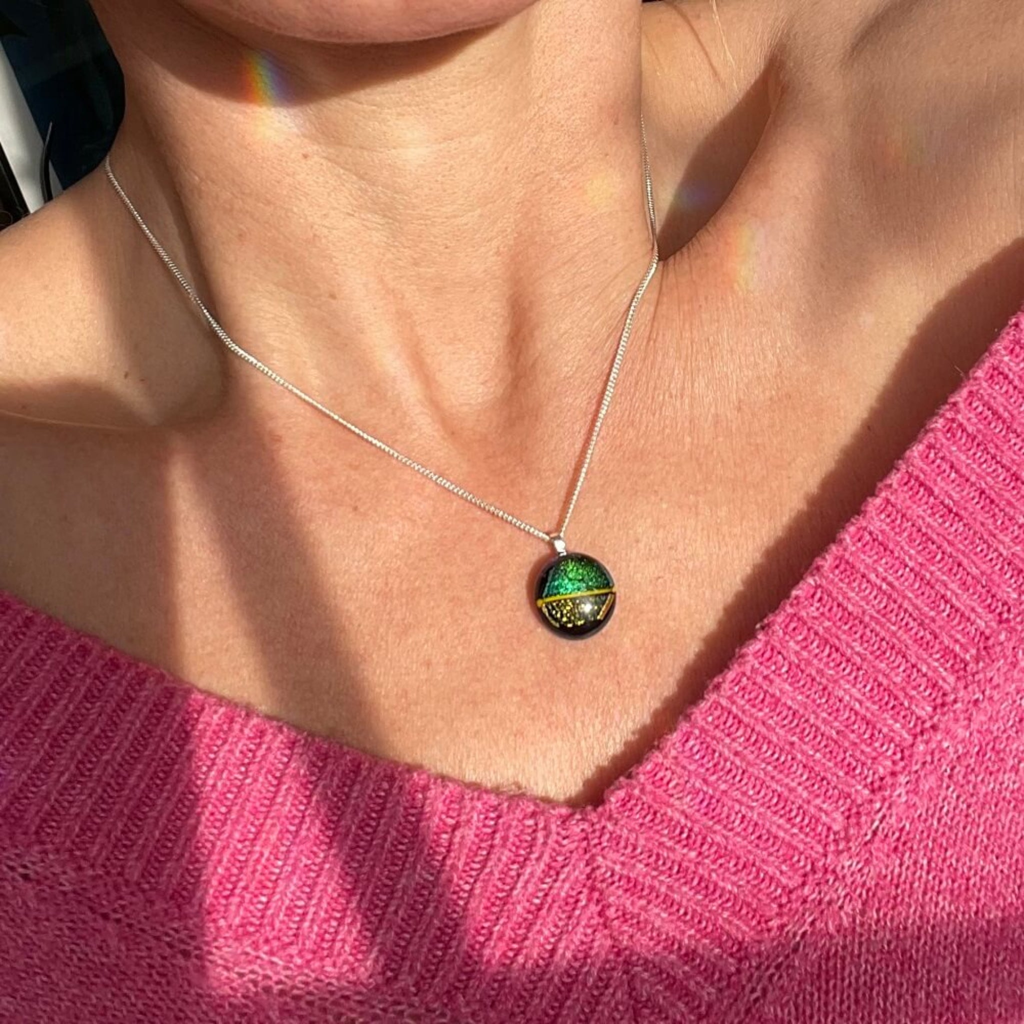 green and gold  glittering dichroic fused glass pendant on sterling silver chain worn by a person in a pink sweater. 