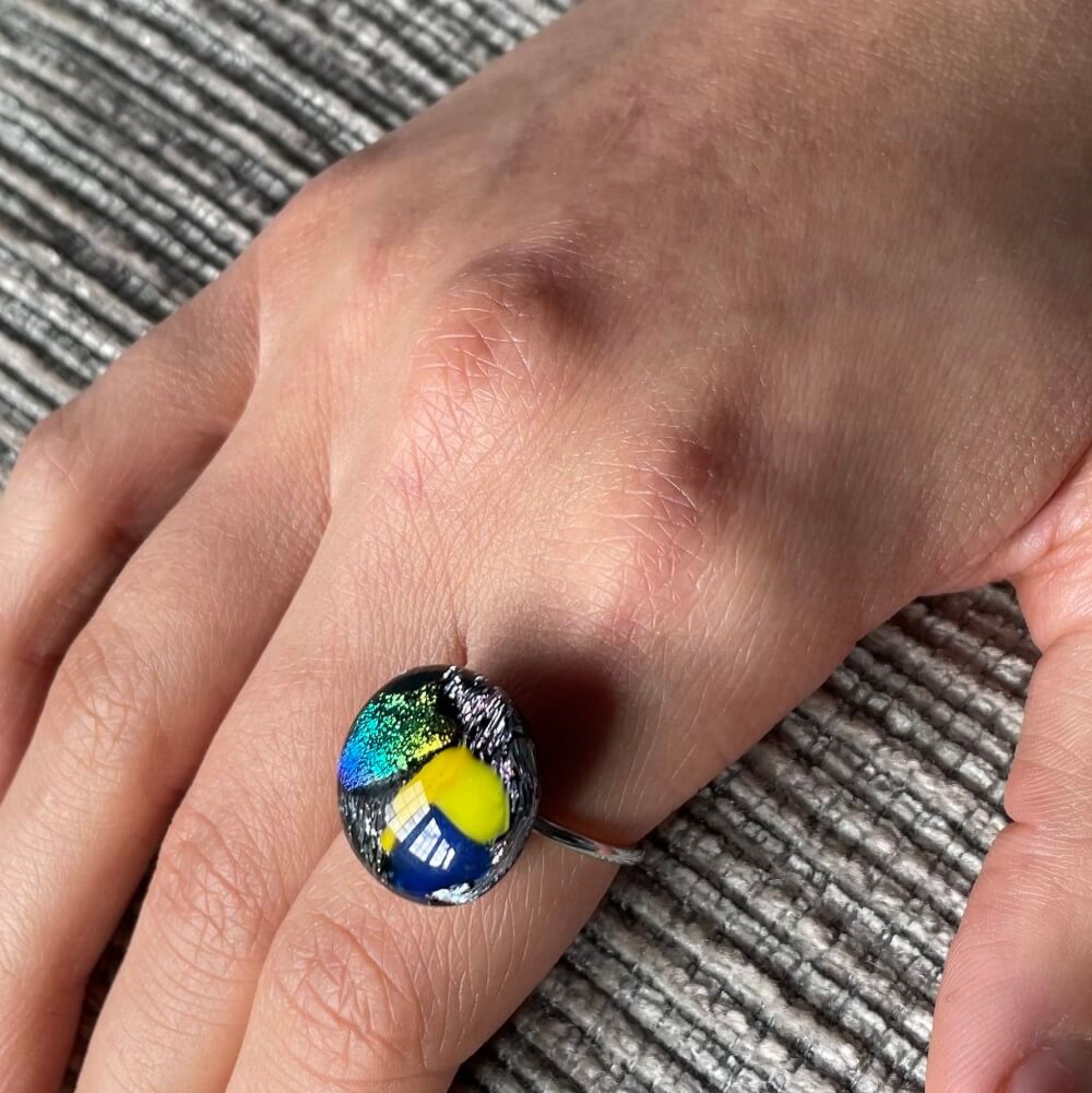 woman wearing a ring in index finger, Close-up of a round jewel statement ring, colourful dichroic fused glass ring, yellow, blue, glittering pink glass, 