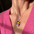 fused glass pedant, colourful pendant worn by a person in a pink sweater. pink, gold, blue, purple glittering dichroic glass, in a sterling silver snake chain.