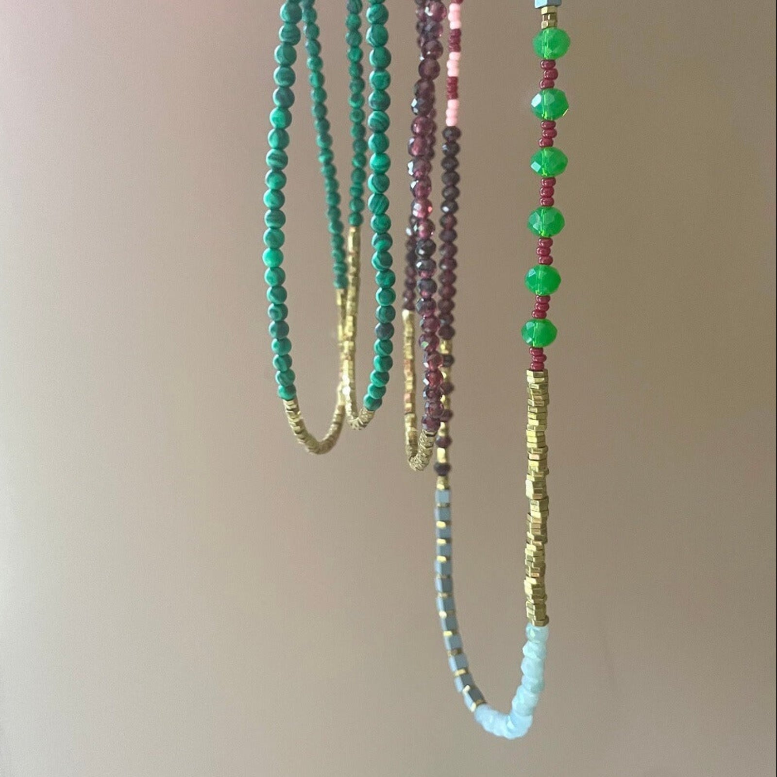 Three beaded necklaces with green, red, and blue beads on a neutral background