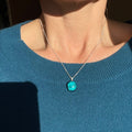 Person wearing a blue sweater with a necklace featuring a handmade, fused glass, turquoise dichroic pendant, on sterling silver elegant box chain.
