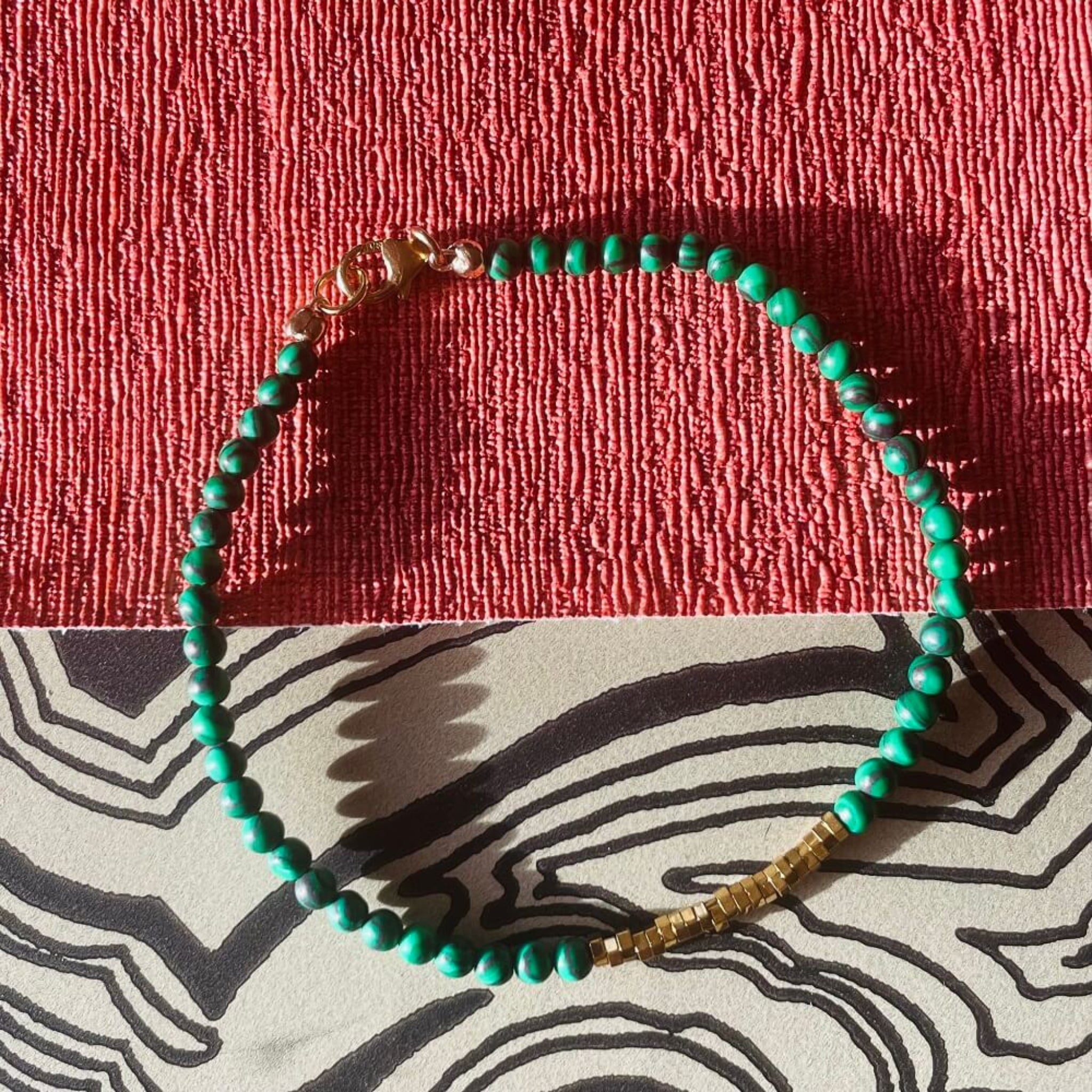 green malachite and gold hematite  beaded bracelet on a textured red and patterned surface, made with 14l rolled gold quality fixtures