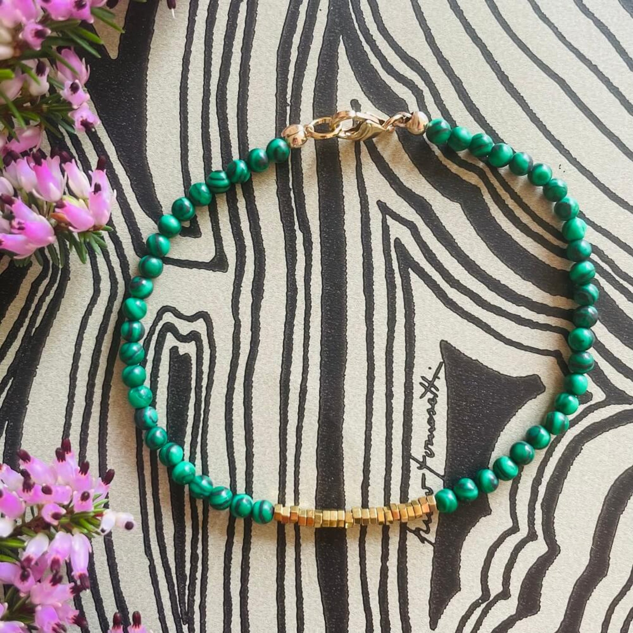 green malachite and gold hematite  beaded bracelet on a patterned black and cream surface, made with 14k rolled gold quality fixtures