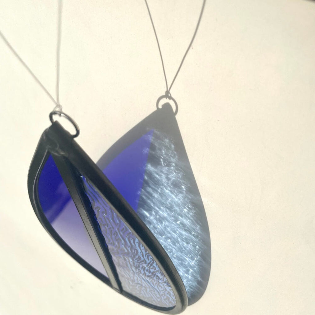 dark blue and light blue hanging stained glass, garden tree spinner or window sun catcher, lovely coloured blue refraction against a cream background.