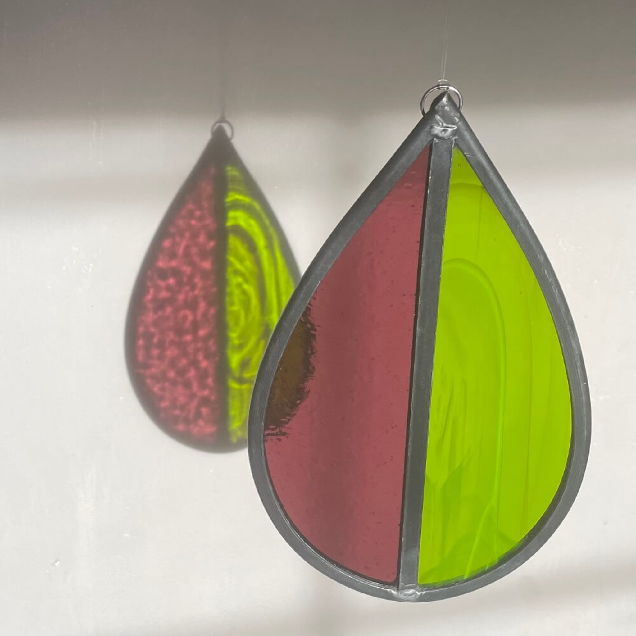 Teardrop-shaped stained glass garden tree spinner or window sun catcher, bright green and purple glass, lovely sunlight fraction on a cream background.