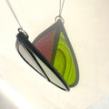 Teardrop-shaped stained glass garden tree spinner or window sun catcher, bright green and purple glass, lovely sunlight fraction on a cream background.