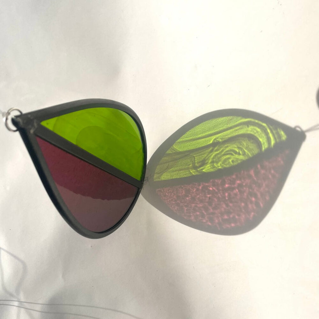Teardrop-shaped stained glass garden tree spinner or window sun catcher, bright green and purple glass, lovely sunlight fraction on a cream background.