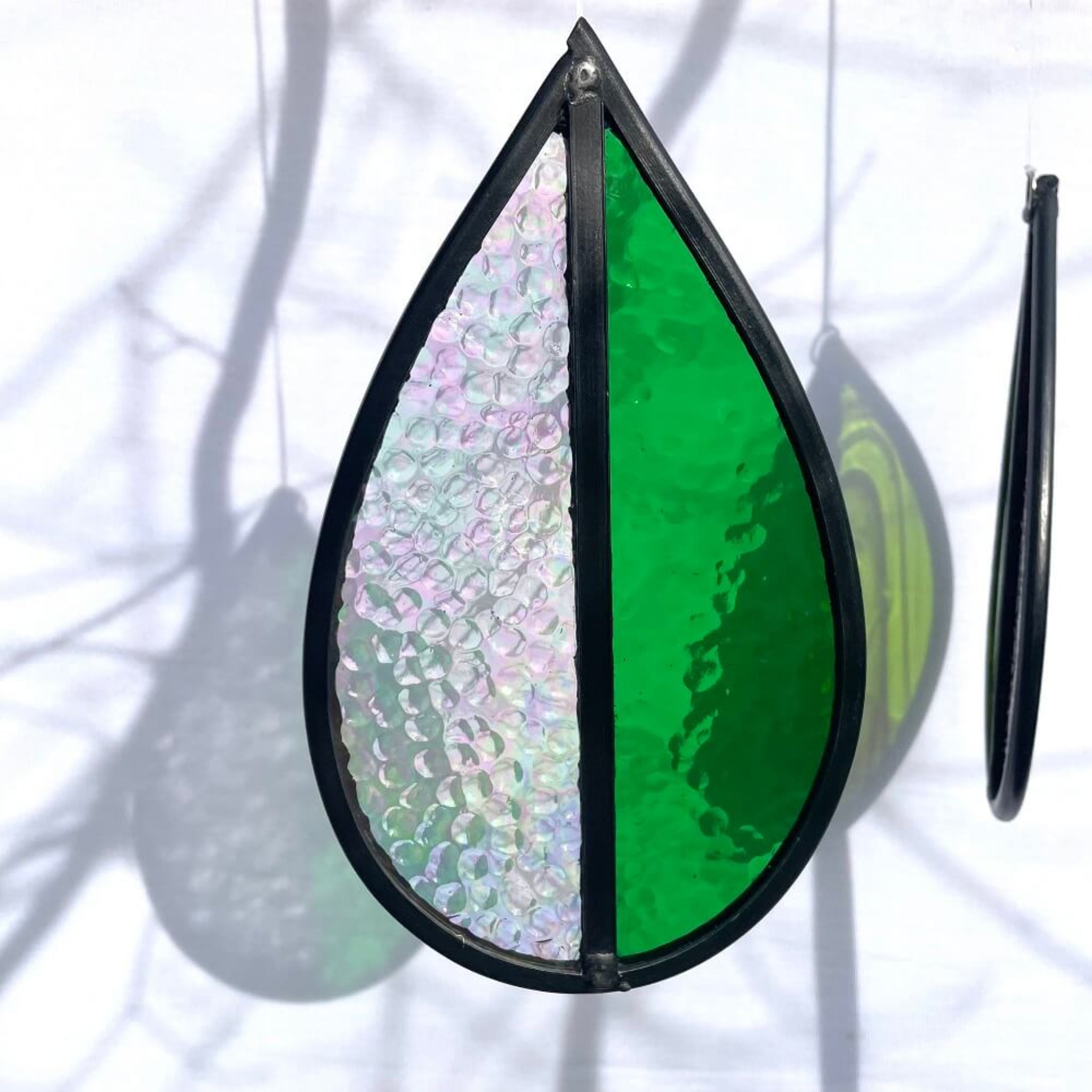 Teardrop-shaped stained glass garden tree spinner or window sun catcher, bright green and clear iridescent glass, hanging against a white background. 