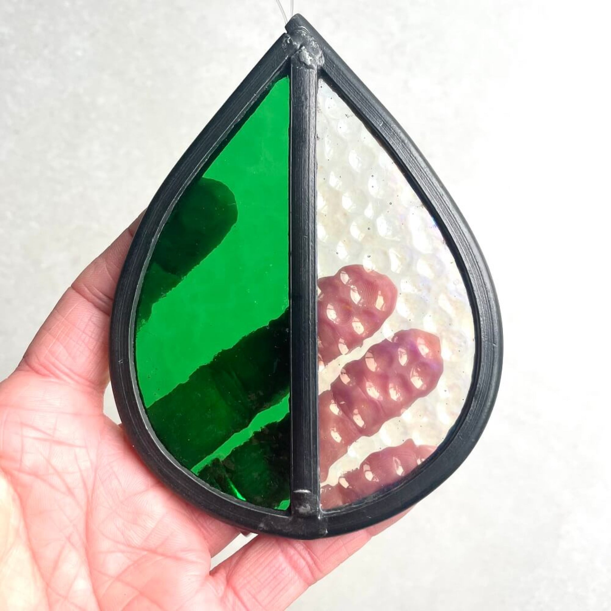 Teardrop-shaped stained glass garden tree spinner / in house sun catcher, with green and clear textured stained glass sections, hand holding it against a white background