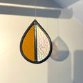 Teardrop-shaped stained glass garden tree spinner / in house sun catcher, with orange and clear, iridescent textured stained glass sections hanging against a white background