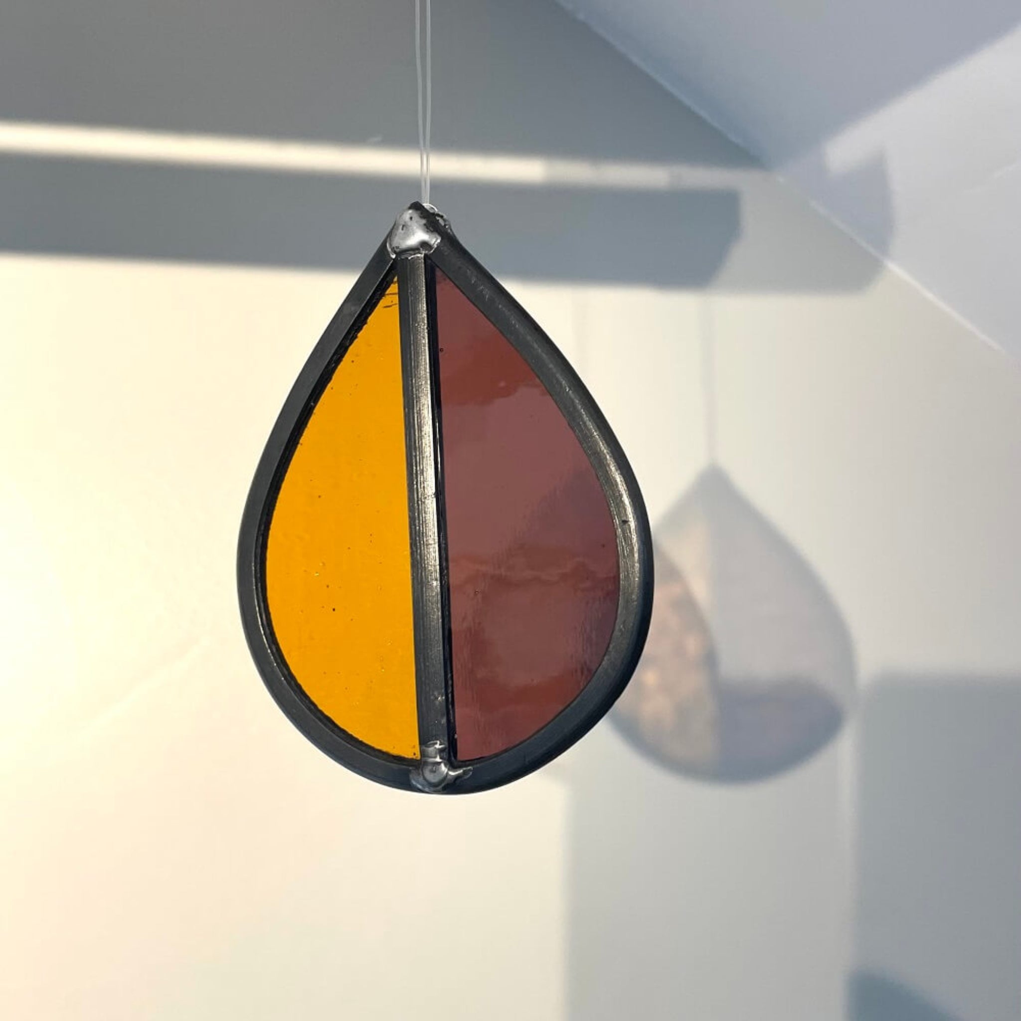 Teardrop-shaped stained glass garden tree spinner / in house sun catcher, with orange and purple stained glass sections hanging against a white background