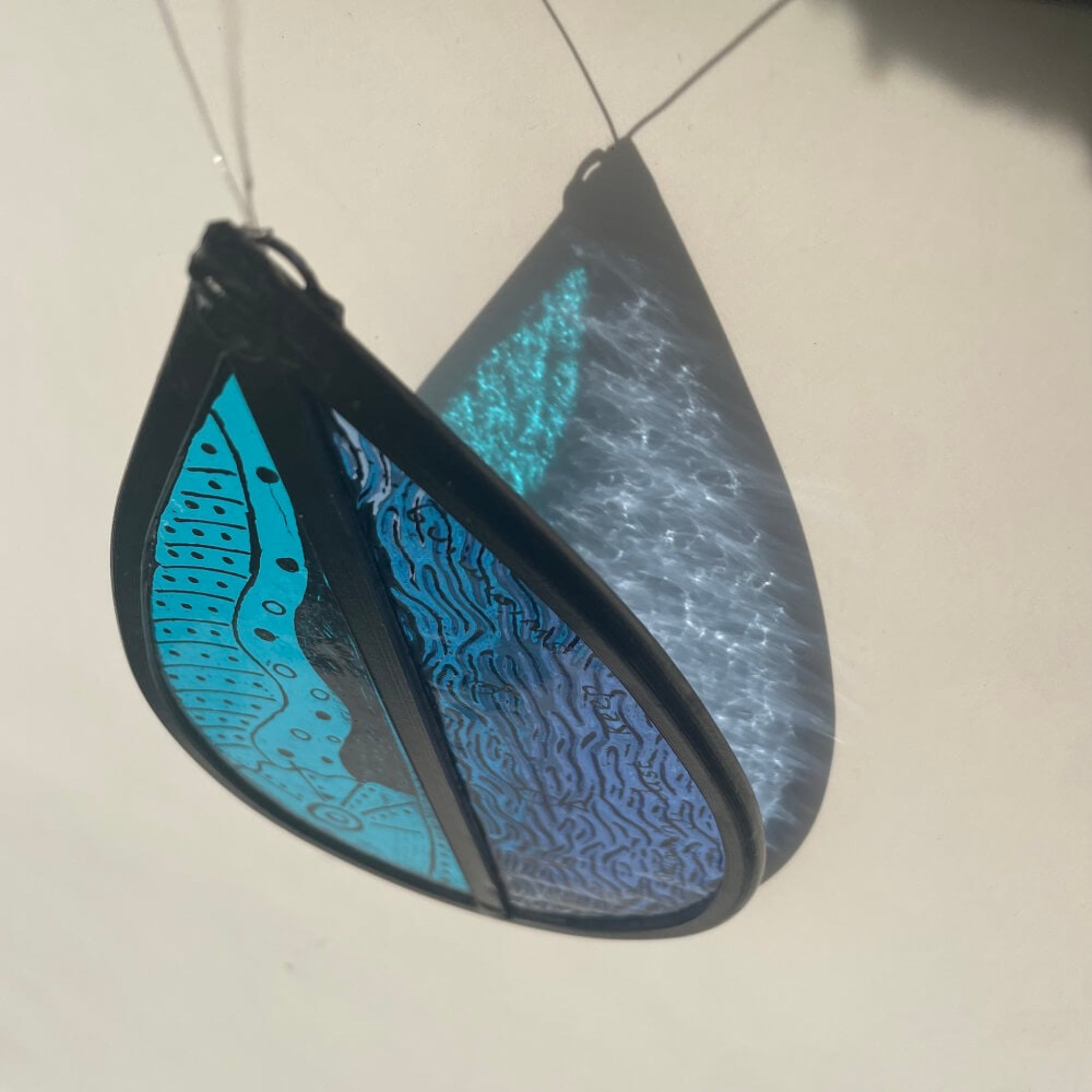 teardrop-shaped stained glass garden tree spinner /  window sun catcher, fish drawing with 'just keep swimming' text,  hanging against a white background. lovely blue sunlight refraction, 