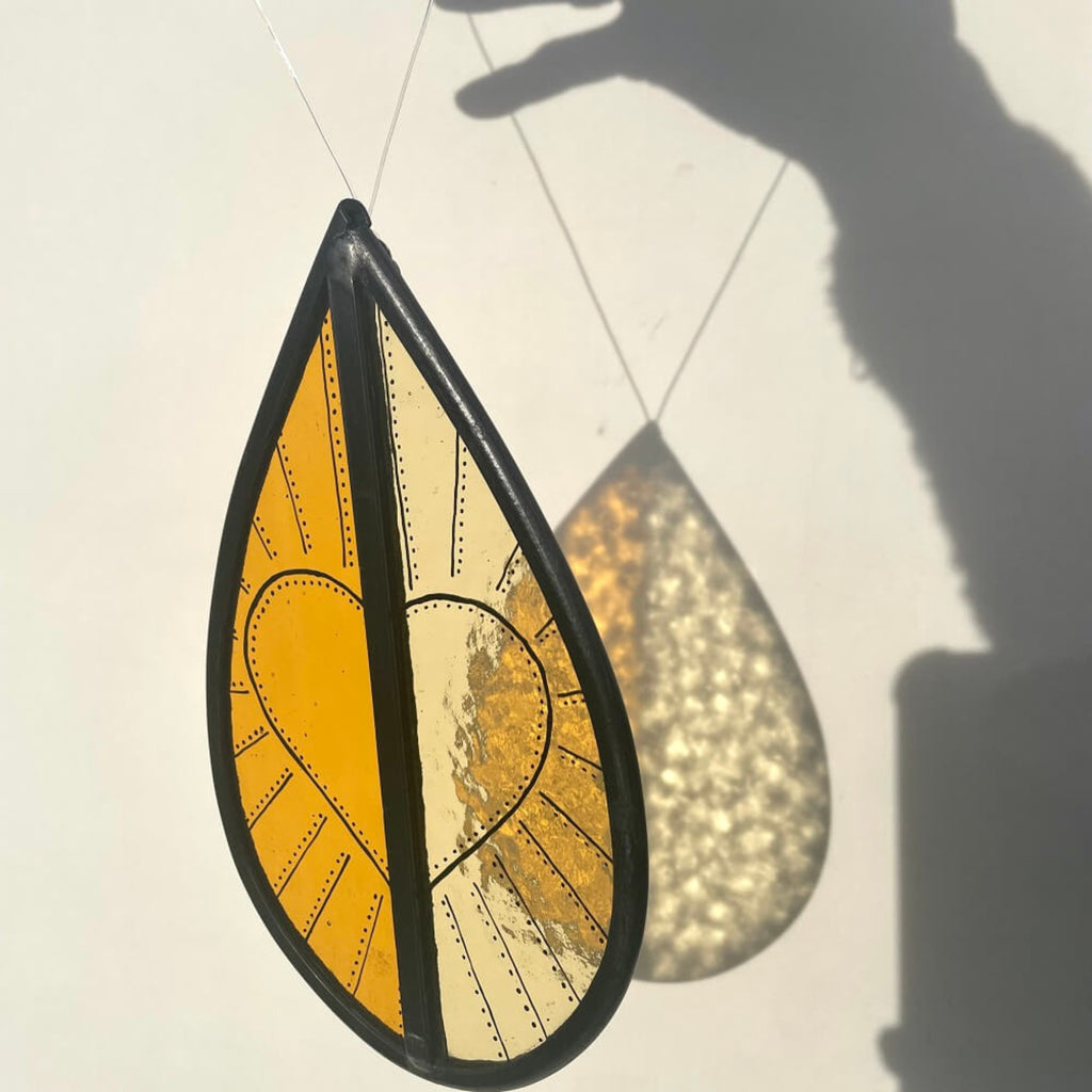 orange and yellow stained glass garden tree spinner, window sun catcher, hand painted heart design on the stained glass hanging on white background.