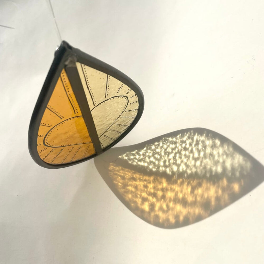 orange and yellow stained glass garden tree spinner, window sun catcher, hand painted heart design on the stained glass hanging on white background, sun light refraction of glass onto background