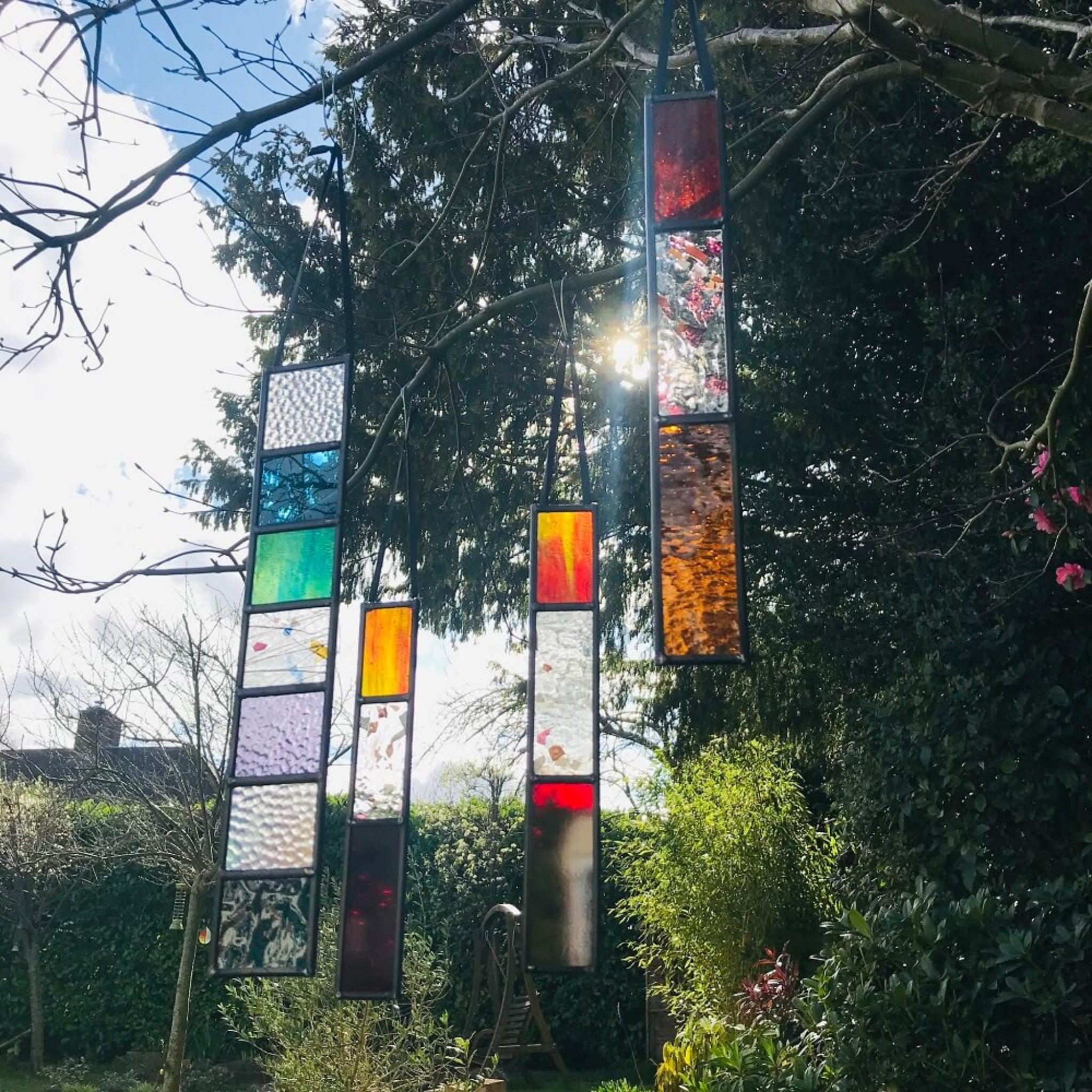 group of 4 decorative long rectangle, red, orange, stained glass garden tree spinner, in house sun catcher, Colourful l stained glass panels hanging outdoors with trees and sky in the background
