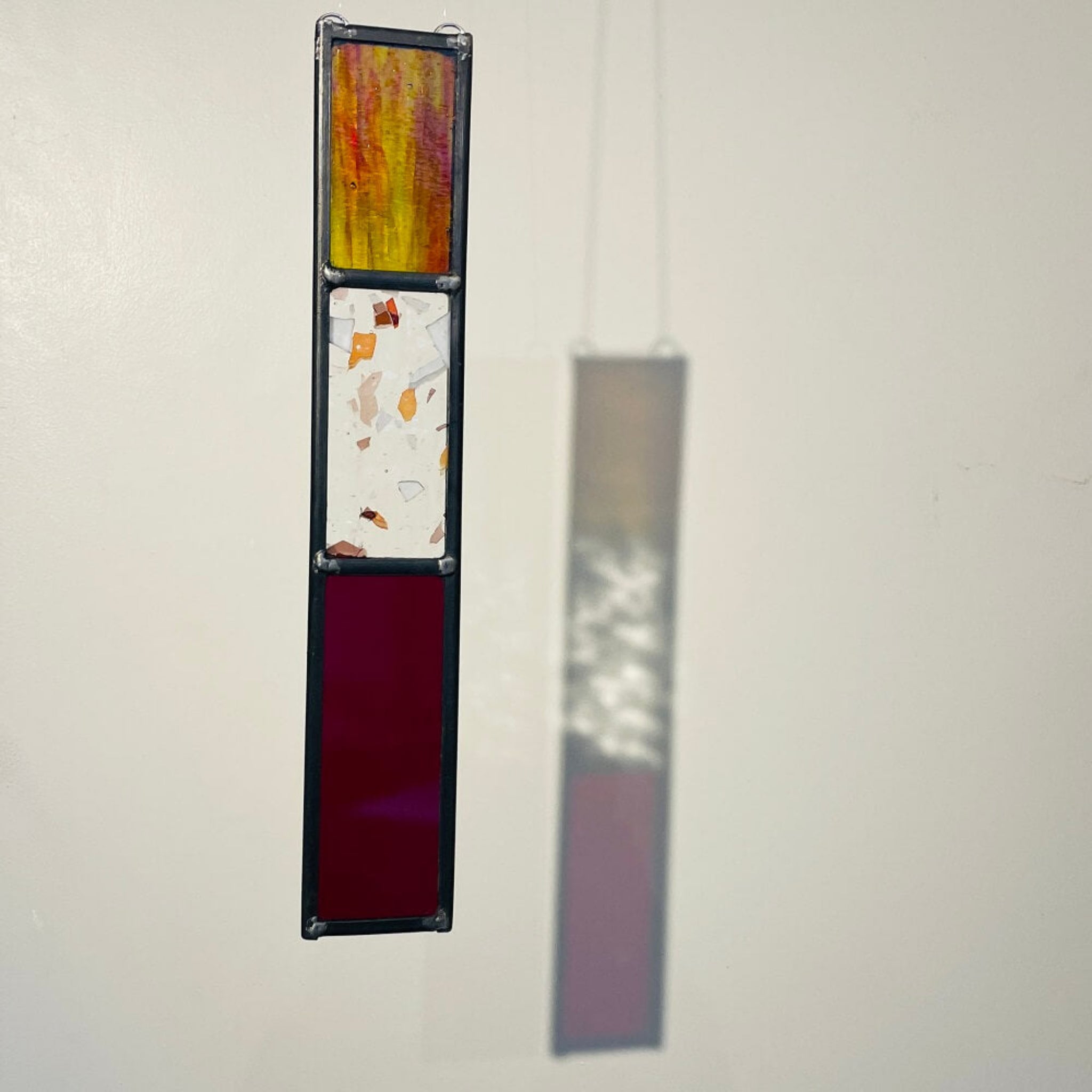 Decorative long rectangle, red stained glass garden tree spinner, in house sun catcher, hanging panel with 3 colourful stained glass sections on a plain background