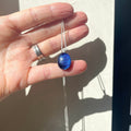 Hand holding a handmade necklace with a fused glass purple dichroic shimmering  pendant, on a sterling silver elegant box chain, against a neutral background