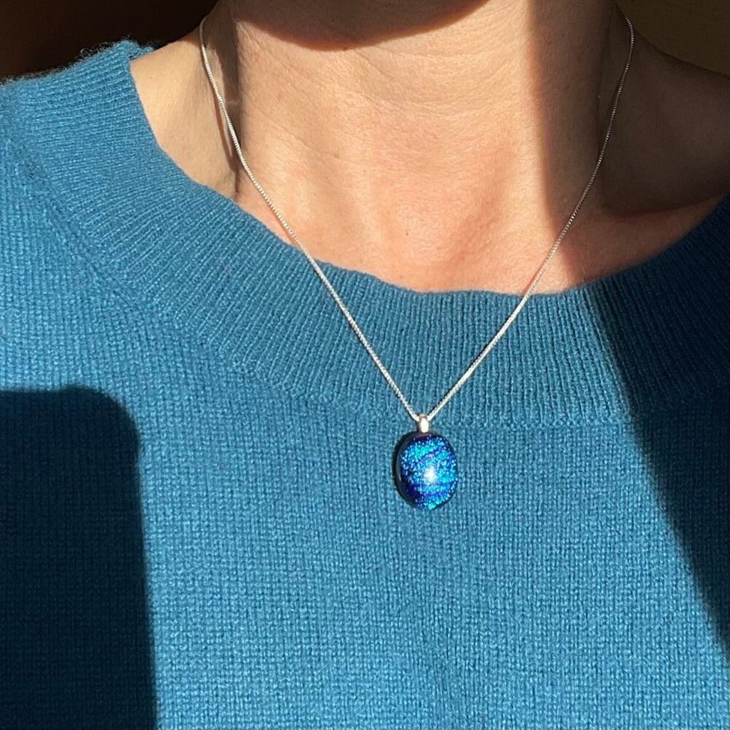 handmade necklace with a fused glass purple dichroic shimmering  pendant, on a sterling silver elegant box chain, woman wearing blue jumper