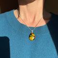 Person wearing a colorful fused glass art pendant, yellow, blue, pink fused glass, with sterling silver chain and bail, necklace against a blue sweater.